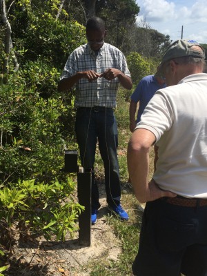 Alex Manda demonstrates for volunteers how to take a groundwater level reading using a handheld meter at a well location in Pine Knoll Shores. Photo: Mark Hibbs